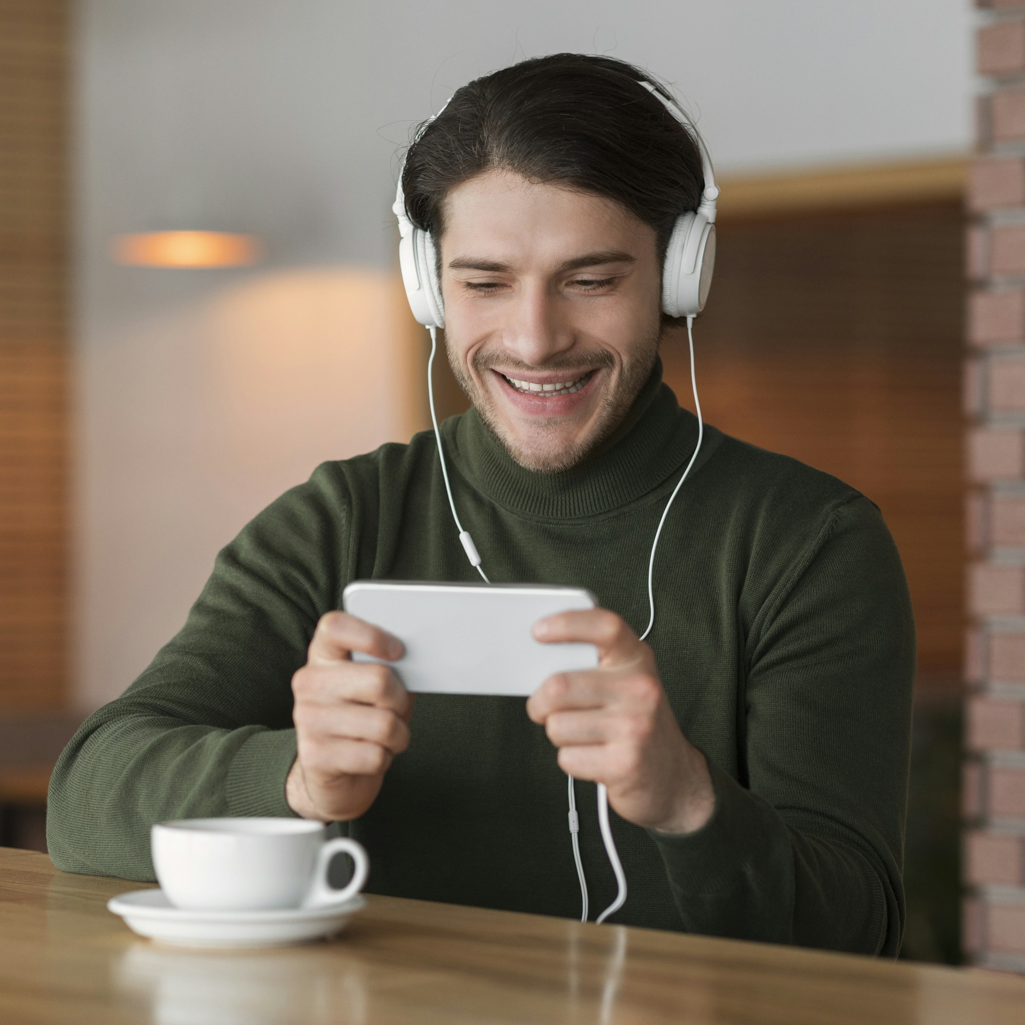 Happy young man in headset using mobile phone at cafe