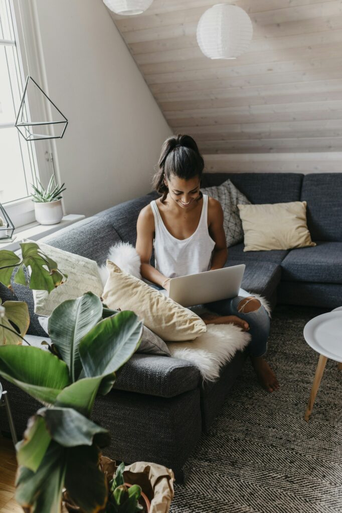 Smiling young woman sitting on the couch at home using laptop