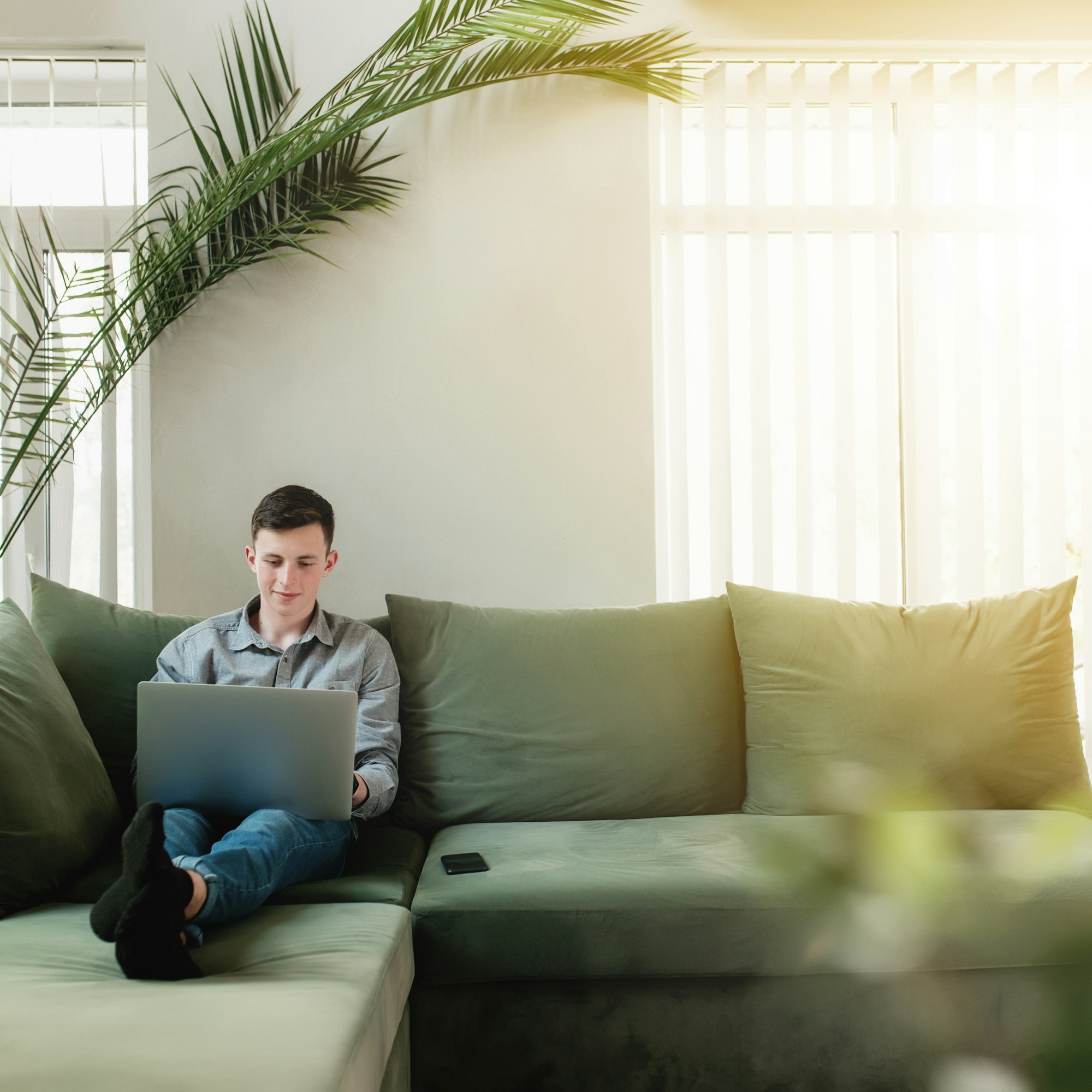 Young guy sitting at green sofa with gray laptop and black phone