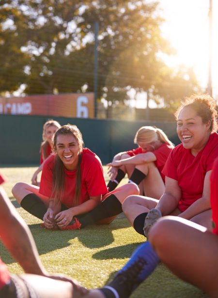 Womens Football Team Stretching Whilst Training For Soccer Match On Outdoor Astro Turf Pitch