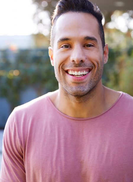 Portrait Of Smiling Hispanic Man In Garden At Home Against Flaring Sun