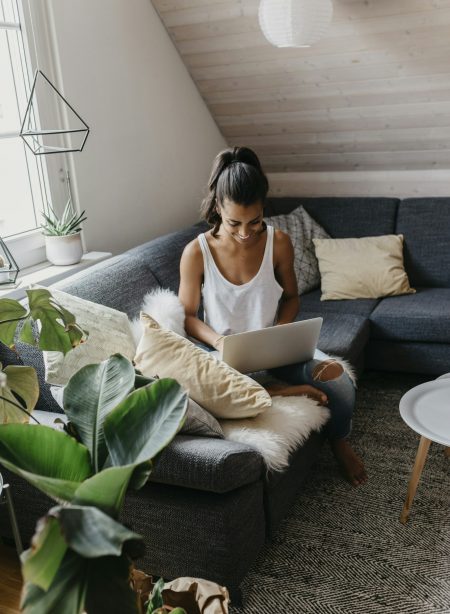 Smiling young woman sitting on the couch at home using laptop